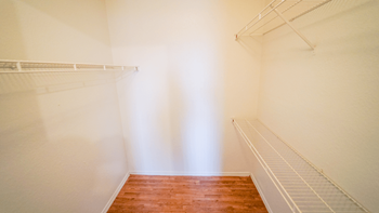 a walk in closet with white walls and a wooden floor